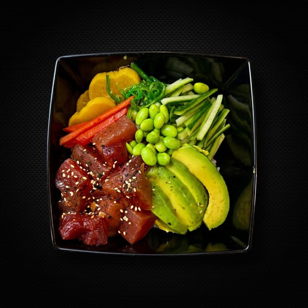 A colorful poke bowl with tuna, avocado, edamame, cucumber, carrots, and seaweed salad.