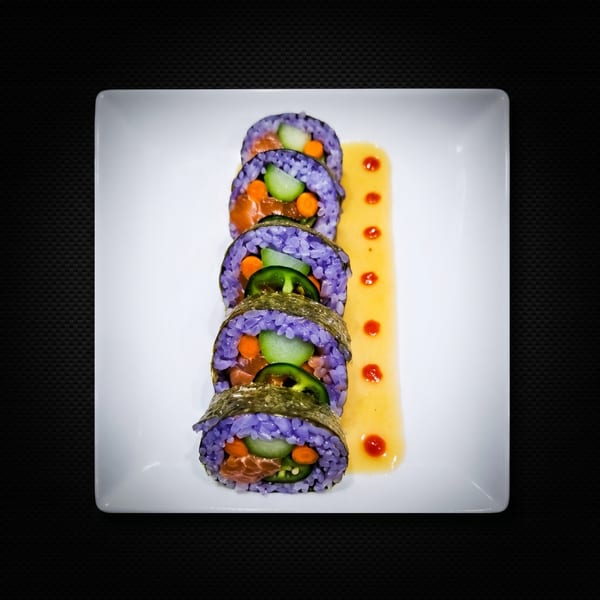 Five pieces of purple sushi with salmon, cucumber, and jalapeño, served with a yellow sauce.