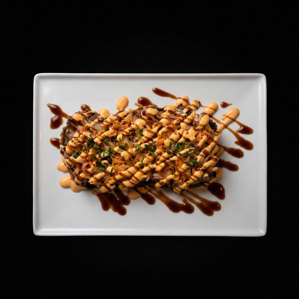 A rectangular white plate holds a dish topped with orange sauce, dark drizzles, and green herbs.