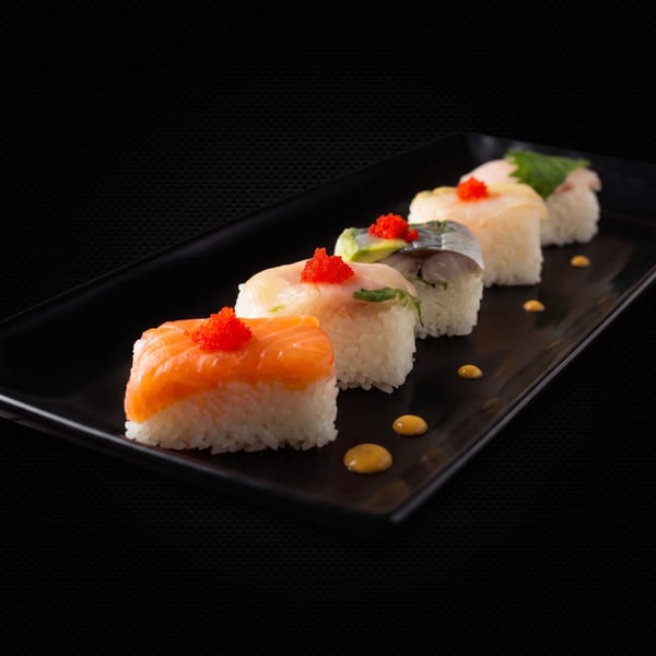 Five pieces of nigiri sushi with various fish and roe on a black rectangular plate.