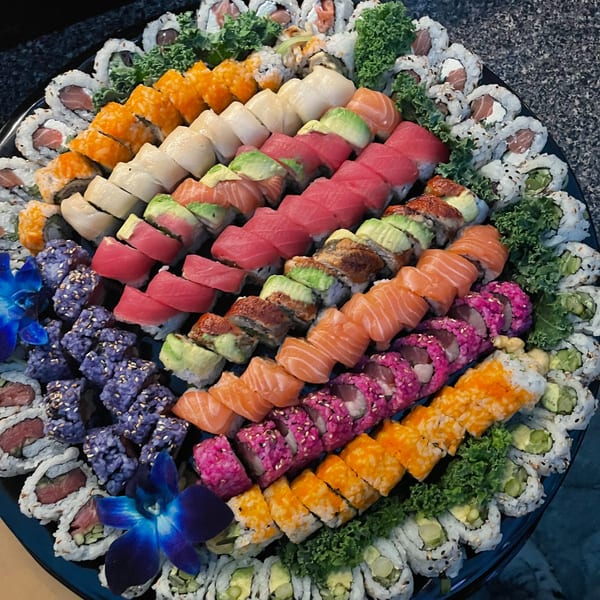 A large platter of colorful sushi rolls, including salmon, tuna, avocado, and roe, garnished with lettuce and blue orchids.