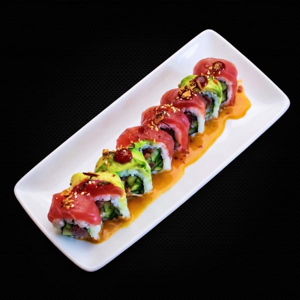 Tuna and avocado sushi rolls with sauce and sesame seeds on a white rectangular plate.