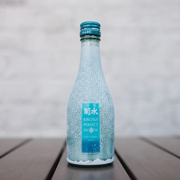 A bottle of Kikusui Perfect Snow sake with a blue label, on a wooden table.