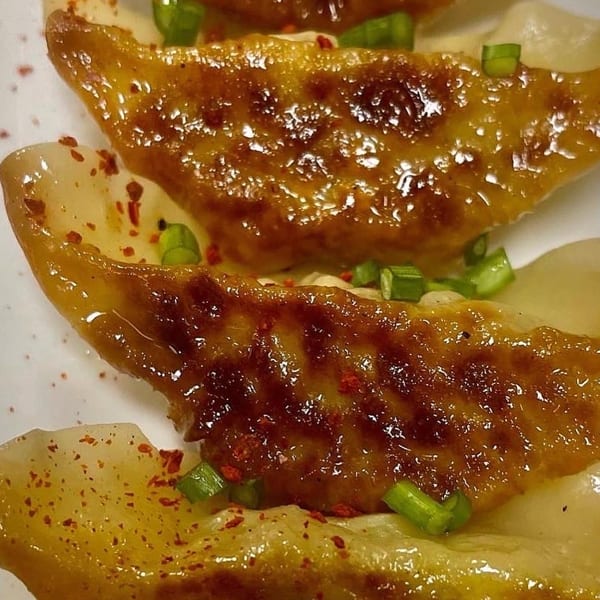 Close-up of golden-brown pan-fried dumplings garnished with chopped green onions and red pepper flakes.