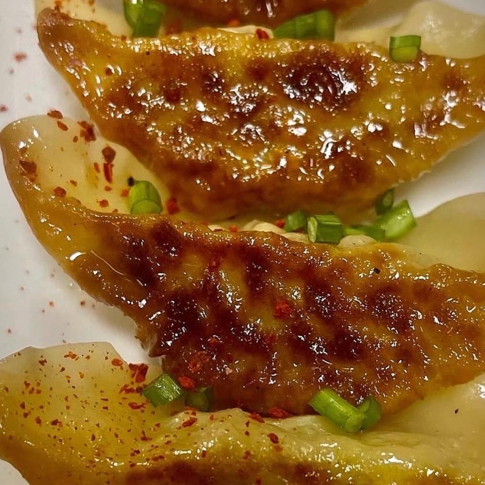 Close-up of golden-brown pan-fried dumplings garnished with chopped green onions and red pepper flakes.